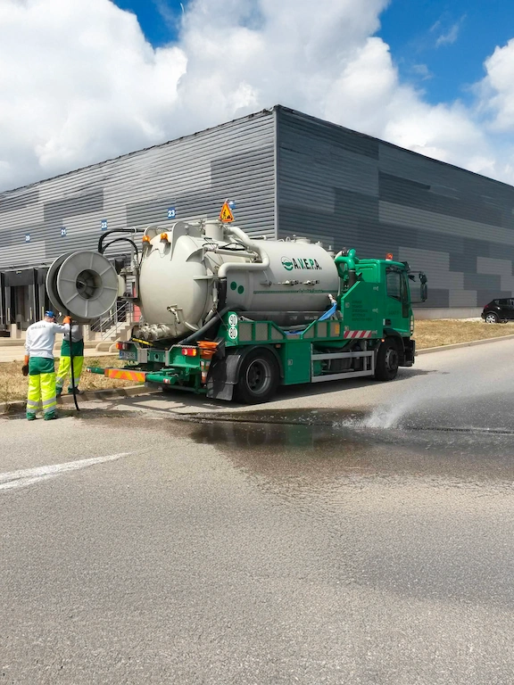 camion assainissement devant immeuble Camion aspirateur de voirie en action près d'entrepôt.