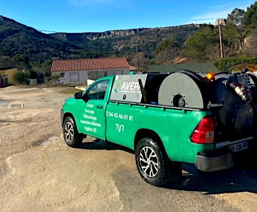 Camion vert de nettoyage stationné, paysage vallonné.